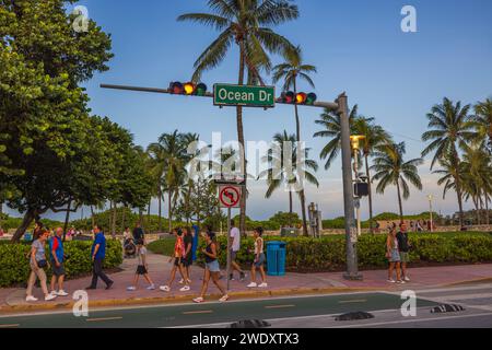 Journée ensoleillée sur Ocean Drive de Miami Beach avec des piétons se promenant le long du trottoir, des arbres verts vibrants, des palmiers et un ciel bleu sans nuages. Miami Banque D'Images