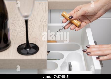 femme tient un tire-bouchon dans sa main pour ouvrir une bouteille de vin. la main d'une femme prend un tire-bouchon dans un tiroir de cuisine. alcoolisme féminin. Haute qualité Banque D'Images