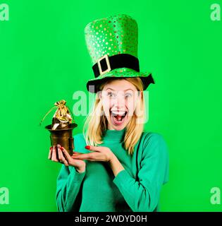 Pot d'argent pour la fête de Patrick. Femme heureuse en chapeau haut de gamme vert avec petit sac d'or. Célébration de la fête des Patricks. Fille souriante en chandail vert et Banque D'Images