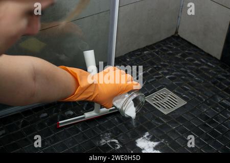 Gros plan des mains d'une femme versant du bicarbonate de soude sur le sol de la douche pour nettoyer, nettoyer et écologique Banque D'Images