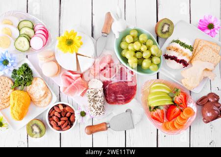 Scène de table de charcuterie thème printemps ou Pâques sur fond de bois blanc. Variété de fromages, viandes, fruits et légumes hors-d'œuvre. Vue de dessus Banque D'Images