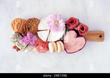 Planche de charcuterie à thème de la fête des mères sur fond de marbre blanc. Variété de fromages, viandes, fruits et hors-d'œuvre sucrés. Vue de dessus. Banque D'Images