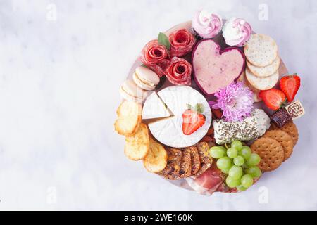 Planche de charcuterie à thème de la fête des mères sur fond de marbre blanc. Assortiment de fromage, viande, fruits et hors-d'œuvre sucrés. Vue de dessus. Banque D'Images