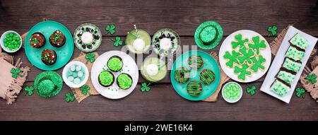 Desserts sur le thème de la Saint-Patrick. Scène de table sur un fond de bannière en bois sombre. Biscuits Shamrock, cupcakes verts, brownies, beignets et bonbons. Top dow Banque D'Images