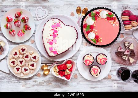 Scène de table de Saint Valentin avec un assortiment de desserts et de bonbons. Vue aérienne sur un fond de bois blanc. Thème amour et coeurs. Banque D'Images