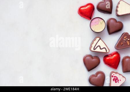 Bordure latérale en chocolat de la Saint-Valentin. Thème coeur rouge et rose. Vue de dessus sur un fond de marbre blanc avec espace de copie. Banque D'Images