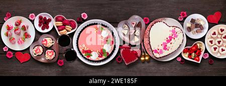 Scène de table de Saint-Valentin avec desserts et bonbons assortis. Vue aérienne sur un fond de bannière en bois sombre. Thème amour et coeurs. Banque D'Images