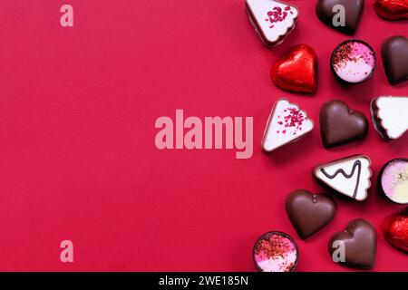 Bordure latérale en chocolat de la Saint-Valentin. Thème coeur rouge et rose. Vue ci-dessus sur un fond de papier rouge avec espace de copie. Banque D'Images