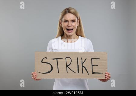 Femme en colère tenant la bannière en carton avec la frappe de mot sur fond gris Banque D'Images