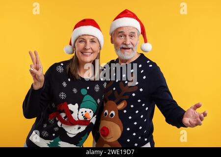 Heureux couple senior dans des pulls de Noël et des chapeaux de Père Noël sur fond orange Banque D'Images