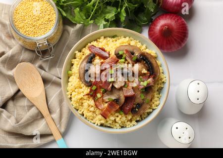 Bouillie de millet savoureuse avec champignons, bacon et oignon vert dans un bol sur une table blanche, mise à plat Banque D'Images