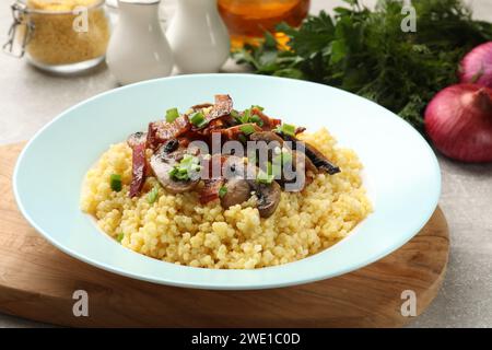 Savoureux porridge de millet avec champignons, bacon et oignon vert sur la table grise, gros plan Banque D'Images