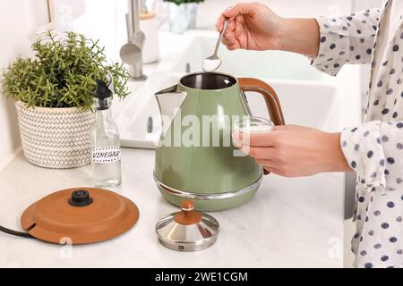 Femme ajoutant du bicarbonate de soude dans une bouilloire électrique dans la cuisine, closeup Banque D'Images