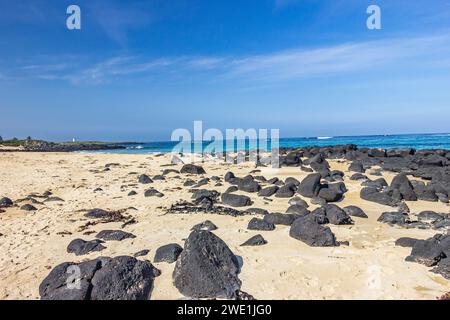 Roches noires éparpillées sur la plage de sable de Griffiths Island de Port Fairy à Victoria, Australie. Banque D'Images