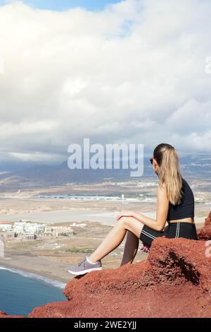 Une photo captivante capturant l'essence de la sérénité, comme une femme devient un avec la nature sur un rocher rouge vibrant surplombant l'océan. Banque D'Images