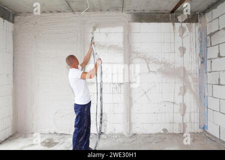 Plâtrage ouvrier plâtrant les murs de la maison, finition des murs avec la machine de plâtre pulvérisé. Chapes murales. Plâtrage avec Banque D'Images