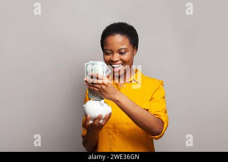 Femme modèle souriante réussie tenant la banque d'argent et le billet de banque en dollar américain sur fond gris Banque D'Images