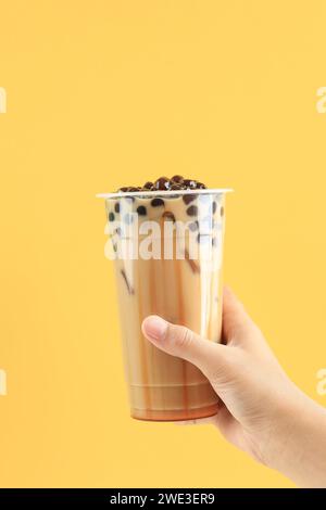 Main féminine Taiwan Boba Pearl Milk Tea avec sirop de sucre de palme liquide sur fond jaune, espace de copie pour le texte Banque D'Images