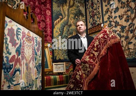 Londres, Royaume-Uni. 23 janvier 2024. Un membre du personnel présente 'a Spanish Velvet Cope', à la fin du 16e siècle, sur le stand textile antiques au London Antique Rug & textile Art Fair (LARTA 2024) à Evolution London à Battersea Park. Textiles rares, tapisseries et tapis, certains datant de plusieurs siècles, sont en vente dans le salon qui se déroule jusqu'au 28 janvier 2024. Crédit : Stephen Chung / Alamy Live News Banque D'Images