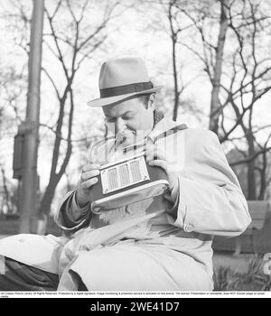 Dans les années 1940 Un homme bien habillé portant un pardessus et un chapeau assorti est assis avec une radio portable à piles pratique qu'il a suspendue à une sangle autour de son cou. Il syntonise la chaîne de radio qu'il veut écouter en tournant un bouton. 1947. Kristoffersson réf. AC8-1 Banque D'Images