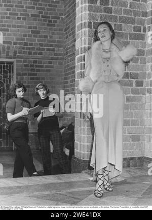 La mode dans les années 1950 Une femme portant une élégante robe blanche avec un long col en fourrure, des gants longs blancs assortis et des sandales gladiateurs. Elle participe au défilé de mode annuel à l'hôtel de ville de Stockholm. Derrière elle se trouvent Barbro Rönn et Lena Claeson, obsédés par la mode, qui dessinent la belle et intéressante robe de soirée. Suède 1952 Banque D'Images