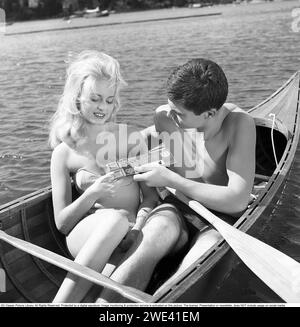 Chocolat Mazetti. Un jeune couple assis ensemble dans un canoë par une journée ensoleillée d'été et il lui offre du chocolat de sa barre de chocolat. Suède 1962. Kristoffersson réf CZ54 Banque D'Images