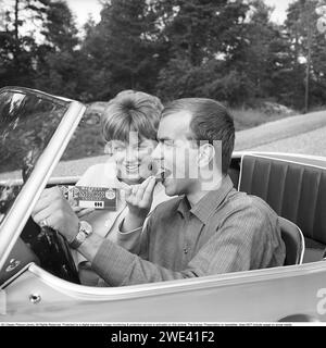 Chocolat Mazetti. Un jeune couple assis ensemble dans une voiture décapotable par une journée ensoleillée d'été et elle offre dim un morceau de chocolat de sa barre de chocolat. Suède 1962. Kristoffersson réf CZ54 Banque D'Images