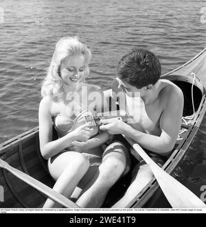 Chocolat Mazetti. Un jeune couple assis ensemble dans un canoë par une journée ensoleillée d'été et il lui offre du chocolat de sa barre de chocolat. Suède 1962. Suède 1962. Kristoffersson réf. CZ55-8 Banque D'Images