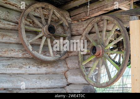 Une vieille roue de chariot en bois pend sur le mur en rondins d'une maison de village. Banque D'Images