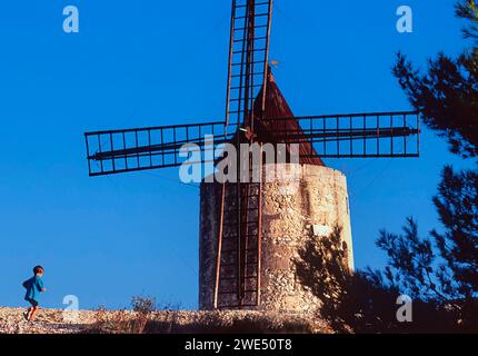 Vieux moulin à vent traditionnel en pierre en Provence France et un garçon en cours d'exécution dans une chemise bleue Banque D'Images