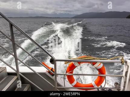 Un anneau de bouées de sauvetage orange d'urgence et la dynamique fluide d'un sillage derrière un catamaran traversier traversant le lac Manapouri, en Nouvelle-Zélande. Banque D'Images