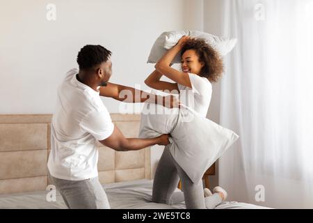 Un couple noir aimant et ludique aime la lutte contre les oreillers insouciante dans la chambre Banque D'Images