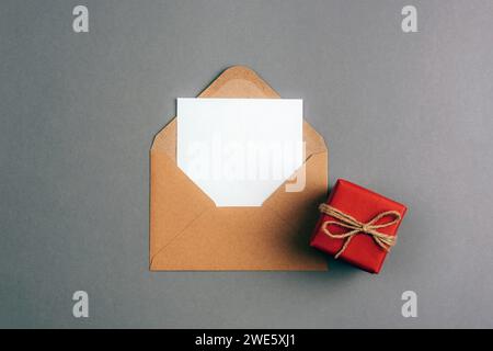 Enveloppe avec carte vierge et boîte cadeau rouge sur fond gris. Saint Valentin, fête de la femme, concept d'anniversaire. Vue de dessus, pose à plat, maquette. Banque D'Images