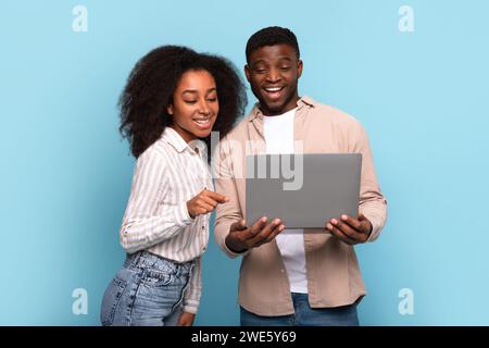 Couple noir s'engageant avec ordinateur portable ensemble sur fond bleu Banque D'Images
