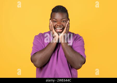 Homme noir excité Cupping visage dans les mains sur fond jaune Banque D'Images