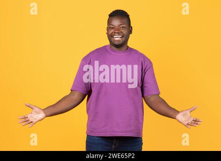 Joyeux Black Guy en T-shirt violet Spreading Arms, fond jaune Banque D'Images