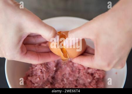 Les mains d'une femme ont battu un œuf en viande, gros plan. Le processus de cuisson de la viande. Banque D'Images