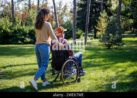 Soignant poussant un homme âgé retraité en fauteuil roulant au parc Banque D'Images