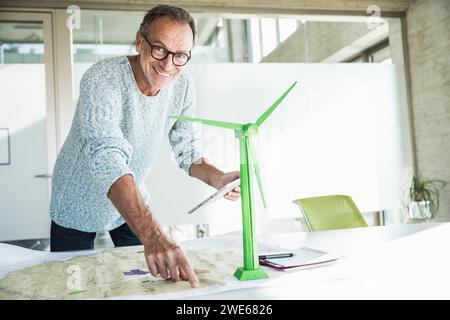 Homme d'affaires souriant pointant sur le plan et tenant la tablette PC près du modèle d'éolienne Banque D'Images