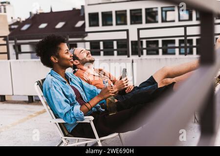 Jeune couple assis avec de la bière sur le toit Banque D'Images