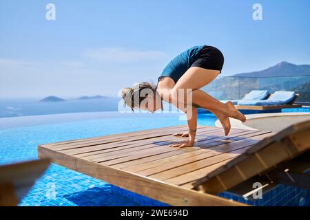 Femme faisant du yoga sur une chaise longue près de la piscine Banque D'Images