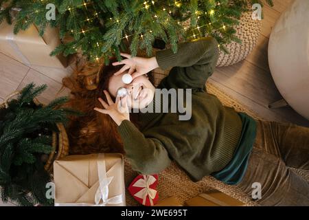 Femme joueuse tenant des ornements de Noël sur les yeux à la maison Banque D'Images