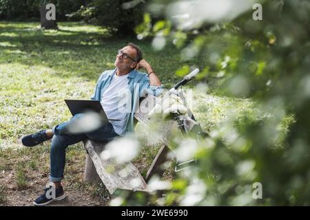 Homme réfléchi avec ordinateur portable assis sur le banc dans le parc Banque D'Images