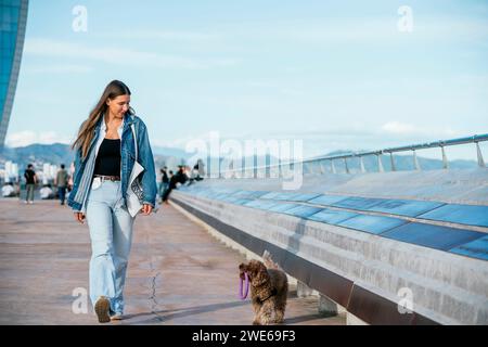 Jeune femme marchant avec le chien caniche dans la rue Banque D'Images