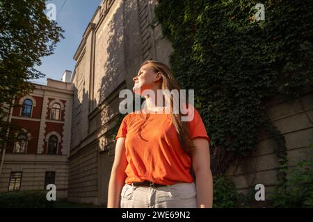 Jeune femme rousse debout devant le bâtiment par jour ensoleillé Banque D'Images