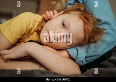 Fille contemplative couchée sur les genoux de sa mère à la maison Banque D'Images