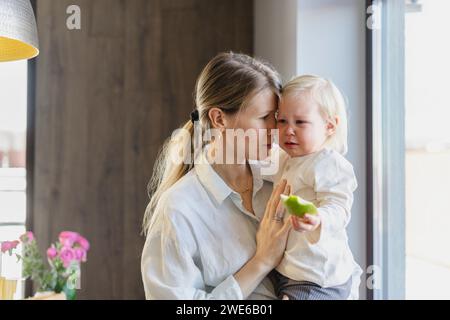Mère consolant fille pleurant près de la fenêtre à la maison Banque D'Images