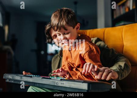 Père souriant enseignant à son fils à jouer du piano électrique à la maison Banque D'Images