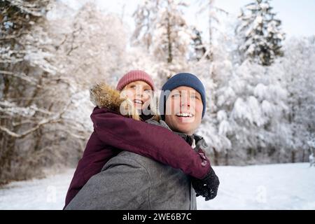 Homme souriant donnant un tour de piggyback à sa fille à la forêt d'hiver Banque D'Images