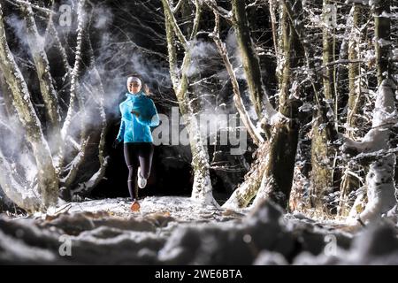 Jeune femme souriante courant près des arbres dans la forêt d'hiver Banque D'Images